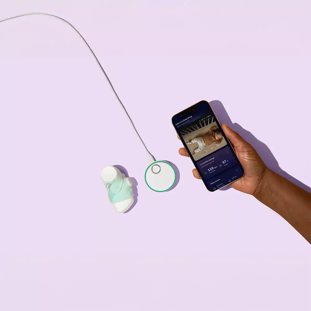 Eine Hand hält ein Smartphone, auf dem eine Babyphone-App angezeigt wird. An das Telefon ist ein Babyüberwachungsgerät in sanftem Grün-Weiß-Design angeschlossen, das ein Baby-Pulsoximeter enthält, das an einem sockenähnlichen Gegenstand befestigt ist, und das alles vor einem hellvioletten Hintergrund.