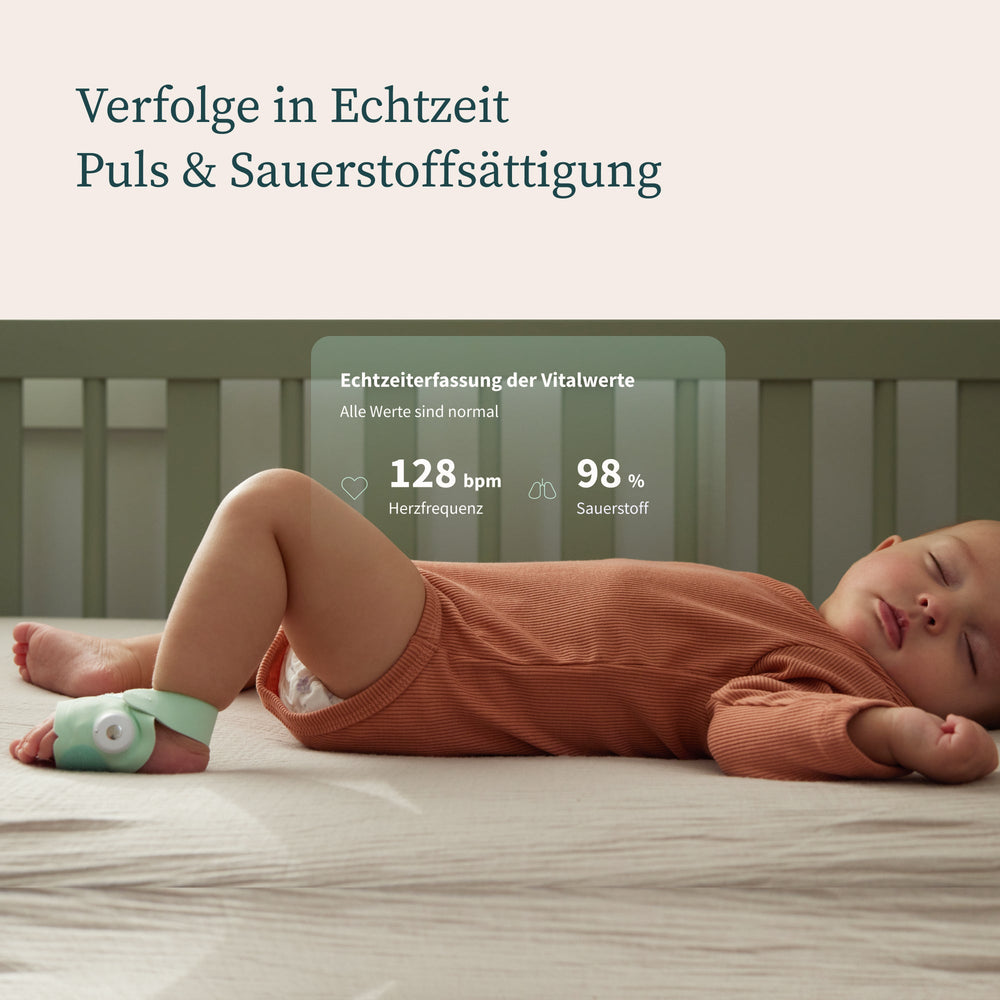 Ein schlafendes Baby in einem rostfarbenen Strampler mit einem grünen Gerät am Fuß. Der Overlay-Text lautet „Verfolge in Echtzeit Puls & Sauerstoffsättigung“ und zeigt eine Herzfrequenz von 128 Schlägen pro Minute und einen Sauerstoffgehalt von 98 %.