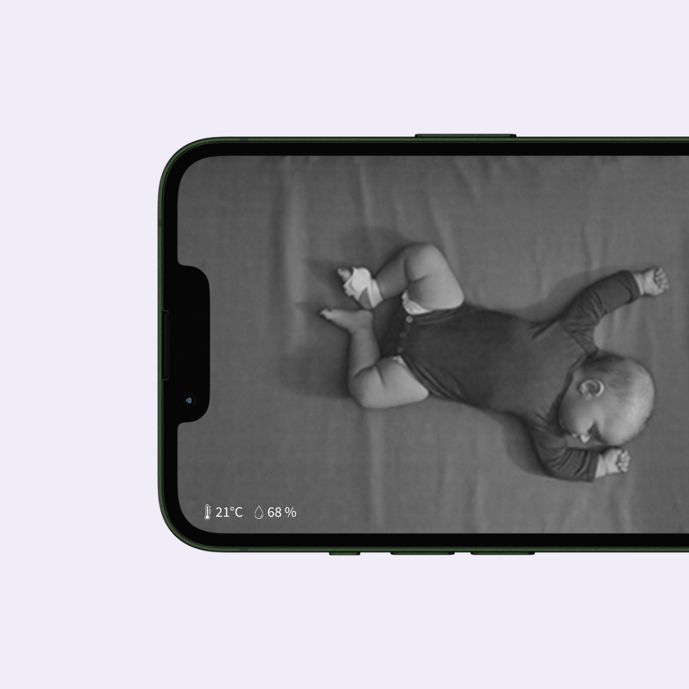 Auf dem Smartphone-Bildschirm ist ein Schwarz-Weiß-Foto eines Babys zu sehen, das mit ausgebreiteten Armen und angewinkelten Beinen auf dem Rücken liegt und per Babyphone überwacht wird. Der Kopf des Babys ist zur Seite gedreht. Auf dem Bildschirm sind außerdem eine Temperatur von 21°C und ein Batteriestand von 68% zu sehen.