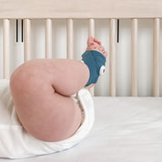 Ein Baby liegt auf einem weißen Laken in einem Kinderbett, wobei nur seine Beine und der Unterkörper zu sehen sind; an einem Fuß trägt es die „Owlet Dream Sock“ mit Ersatzsocke von Owletcare.de.