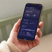 Eine Hand hält ein Smartphone, auf dem die App „Owletcare.de Owlet Dream Sock mit Ersatzsocke“ angezeigt wird, die Gesundheitsdaten, detaillierte Informationen zu den Schlafphasen und ein Balkendiagramm der Schlafzyklen auf einem dunklen Bildschirm anzeigt.