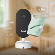 Das „Owlet Dream Duo mit Ersatzsocke“ von Owletcare.de wird abgebildet, bestehend aus einer Babyphone-Kamera und einem mintgrünen Wearable-Sensor. Symbole zeigen die WLAN-Verbindung, die Raumtemperatur (20 °C), die Luftfeuchtigkeit (52 %), die Herzfrequenz (91 Schläge pro Minute) und die Sauerstoffsättigung (98 %) an. Der Hintergrund des Kinderzimmers erscheint unscharf.