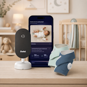 Ein „Owlet Dream Duo“ von Owletcare.de mit Ersatzsöckchen – bestehend aus einer Babyphone-Kamera, zwei tragbaren Babysöckchen und einem Smartphone, auf dem die App für Schlaf- und Vitaldaten angezeigt wird – steht auf einem Holztisch in einem sanft beleuchteten Kinderzimmer mit einem Kinderbett, Plüschtieren und einer neutralen Einrichtung.