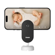 Ein Baby schläft auf einem Bett, dargestellt in scharfem 2K HD Video auf einem Smartphone mit der Owletcare.de Owlet Dream Sight: Neue 2K HD Babyphone Kamera. Sowohl die Kamera als auch das Telefon stehen aufrecht vor einem weißen Hintergrund.